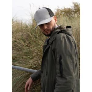 A grey marle cap with a mesh back worn by a man in a green jacket, standing near grassy terrain.