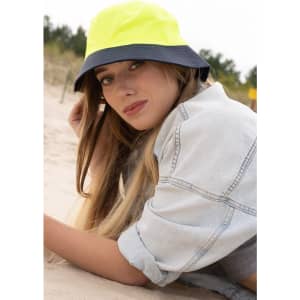 A luminescent yellow and navy bucket hat with a logo, resting on the sand beside a woman.