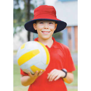 A red and navy reversible bucket hat worn by a smiling boy holding a volleyball, set outdoors.