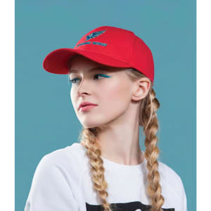 A red cotton twill cap with a buckle, featuring a logo, worn by a model with braided hair against a blue background.