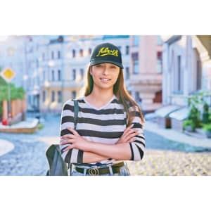 A woman stands confidently on a cobblestone street, wearing a black cap and a striped long-sleeve top.