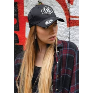 A black twill cap with a logo, worn by a model with long hair, against a graffiti background.