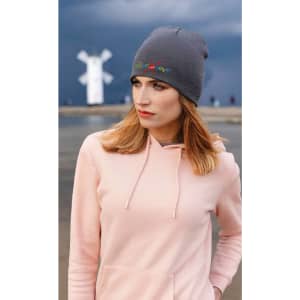 A woman wearing a grey recycled roll down beanie, paired with a light pink hoodie, against a moody backdrop.
