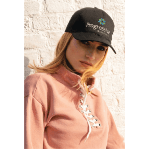A black organic brushed heavy cotton cap with a logo, worn by a model in a pink pullover against a white wall.