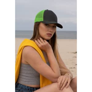 A black and neon green cap with a mesh back, worn by a model seated on a beach, dressed casually.