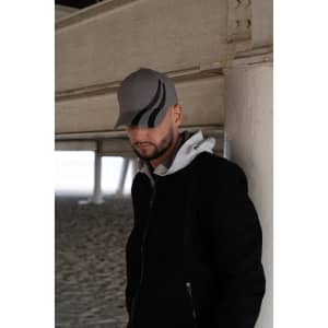 A grey cap with black tyre track designs, worn by a person in a black jacket and grey hoodie under a structure.