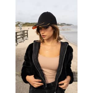 A black cap with a hi-vis orange peak worn by a woman on a beach, in a casual outfit and standing near a boardwalk.