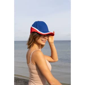 A tri-coloured cap in blue, red, and white, featuring a logo, worn by a woman at the beach.