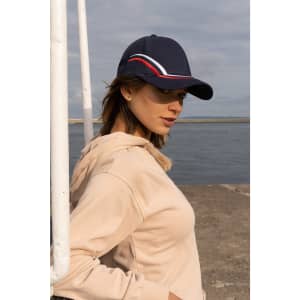 A navy cap with curved embroidery in red and white, worn by a woman near a waterfront.