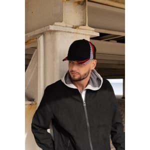 A man wearing a black cap with red and white checks, standing under a structure by the beach.