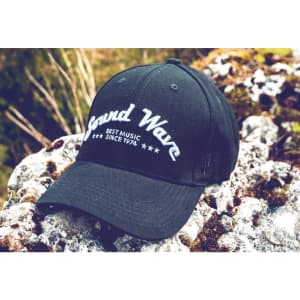 A black cap with a white embroidered logo, featuring the words "Sound Wave" and stars, resting on rocky terrain.