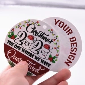 A double-sided round acrylic Christmas ornament featuring festive designs in red, green, and white with a branding logo.