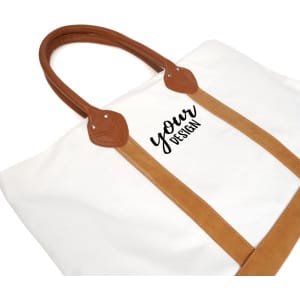 A large canvas tote bag in cream with tan leather handles and an area for personal design.