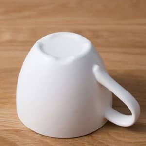 A white porcelain coffee cup featuring a handle, viewed from the bottom on a wooden surface.