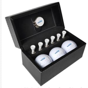 A golf ball set featuring three white golf balls and six white tees, housed in a black leather box with a logo.