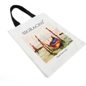 A white canvas tote bag with a black handle and an artistic design featuring a boat by the water. It includes a logo.