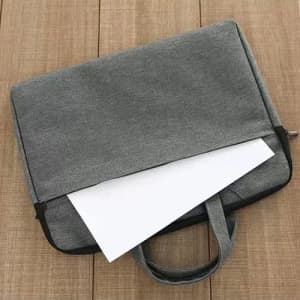 A grey multifunctional briefcase bag on a wooden surface, partially open with a document inside. It features a handle and a logo.