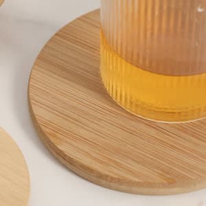 A drink bottle sits on a round, natural bamboo coaster with a smooth finish.