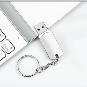 A rotating USB flash drive keychain in silver connected to a laptop keyboard.