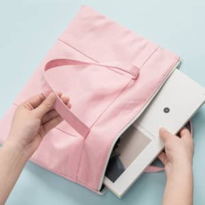 A pink multilayered canvas file bag with a handle, open to reveal a document inside. Features branding.
