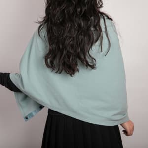 A solid colour button shawl in soft blue worn over a black outfit, showcasing its draped design.