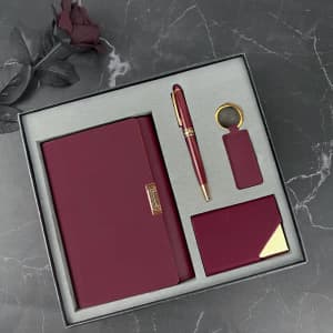 A burgundy gift set featuring a notebook, pen, keyring, and cardholder, presented in a sleek box with a soft interior.