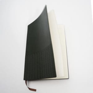 A lined notebook journal in dark green with a textured cover and cream-coloured pages, featuring a ribbon marker.