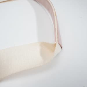 A close-up of a cream-coloured canvas strap with a pink trim, featuring a textured finish.