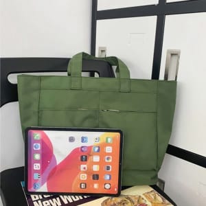 A large green shoulder tote next to a tablet and magazines, featuring front pockets and sturdy handles.