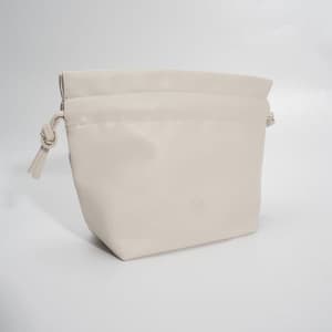 A drawstring makeup bag in a soft cream colour, featuring a logo and a stylish design.