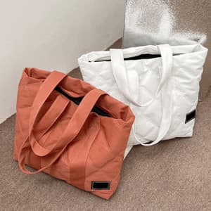 Large puffer tote handbags in orange and white, featuring sturdy handles and a quilted design.