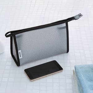 A clear, black mesh makeup bag with a zip top, resting next to a smartphone on a white tiled surface.