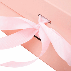 A pink collapsible gift packaging box with a ribbon tied in a bow. It has a logo on the side.
