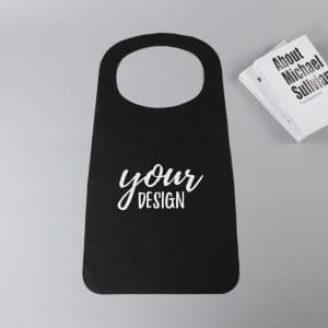 A black disposable non-woven apron with a rounded neck design and a logo, alongside some books.