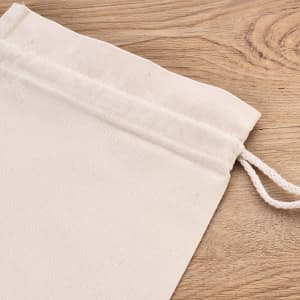 A cream cotton storage bag with a drawstring closure, placed on a wooden surface.