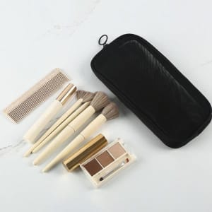 A black mesh toiletry bag with cosmetic brushes, a comb, and an eyeshadow palette arranged on a flat surface.