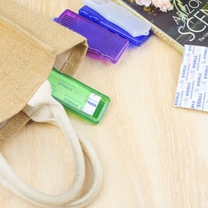 A storage container in green with adhesive bandages, alongside purple and blue items, in a tan bag on a wooden surface.