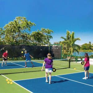 A vibrant outdoor scene featuring four people playing pickleball on a blue and green court surrounded by greenery.