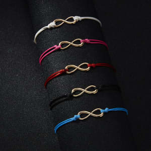 A set of braided infinity-shaped bracelets in white, pink, red, black, and blue, featuring gold-coloured symbols.