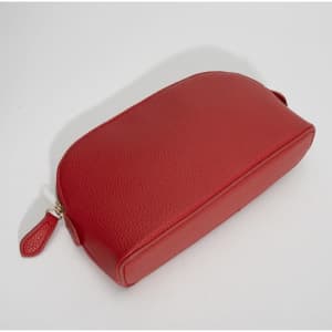 A red shell-shaped cosmetic bag with a textured finish and a zipper opening. It has a small textured zipper pull.