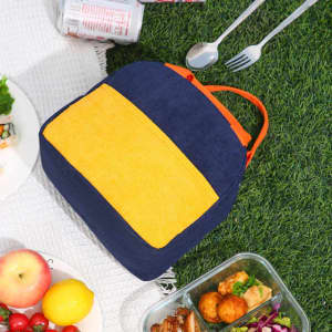 A corduroy insulated lunch bag in navy blue and yellow with an orange zipper, placed on grass beside food items.
