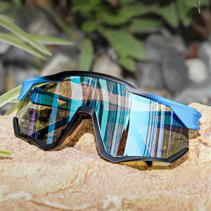 Polarized sports glasses with a blue frame and reflective lenses, resting on a rocky surface among greenery.