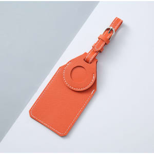 An orange leather luggage tag with a circular attachment and stitching detail. It has a branding logo.