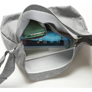 A grey canvas shoulder bag with a visible interior containing a tablet, a wallet, and a drink bottle.