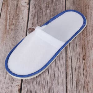 A white non-slip disposable slipper with a blue trim, placed on a wooden surface.
