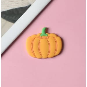 A pumpkin-shaped magnet in vibrant orange with a green stem on a pink background.