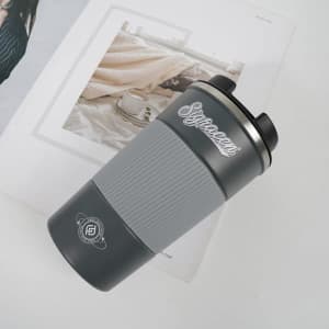 A stainless steel coffee cup in grey, featuring a ribbed design and a logo, resting on a flat surface.
