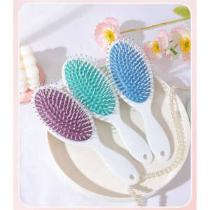 Three custom full-colour paddle hair brushes in purple, teal, and light blue, resting on a white plate with decorative items.