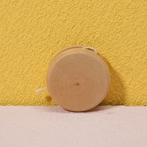 A natural wooden yoyo sits against a yellow wall, showcasing its smooth, circular design.