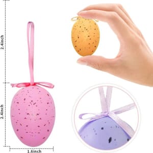 A hand holds an orange speckled Easter egg, alongside a pink speckled egg with a ribbon. Both eggs are for outdoor hanging.